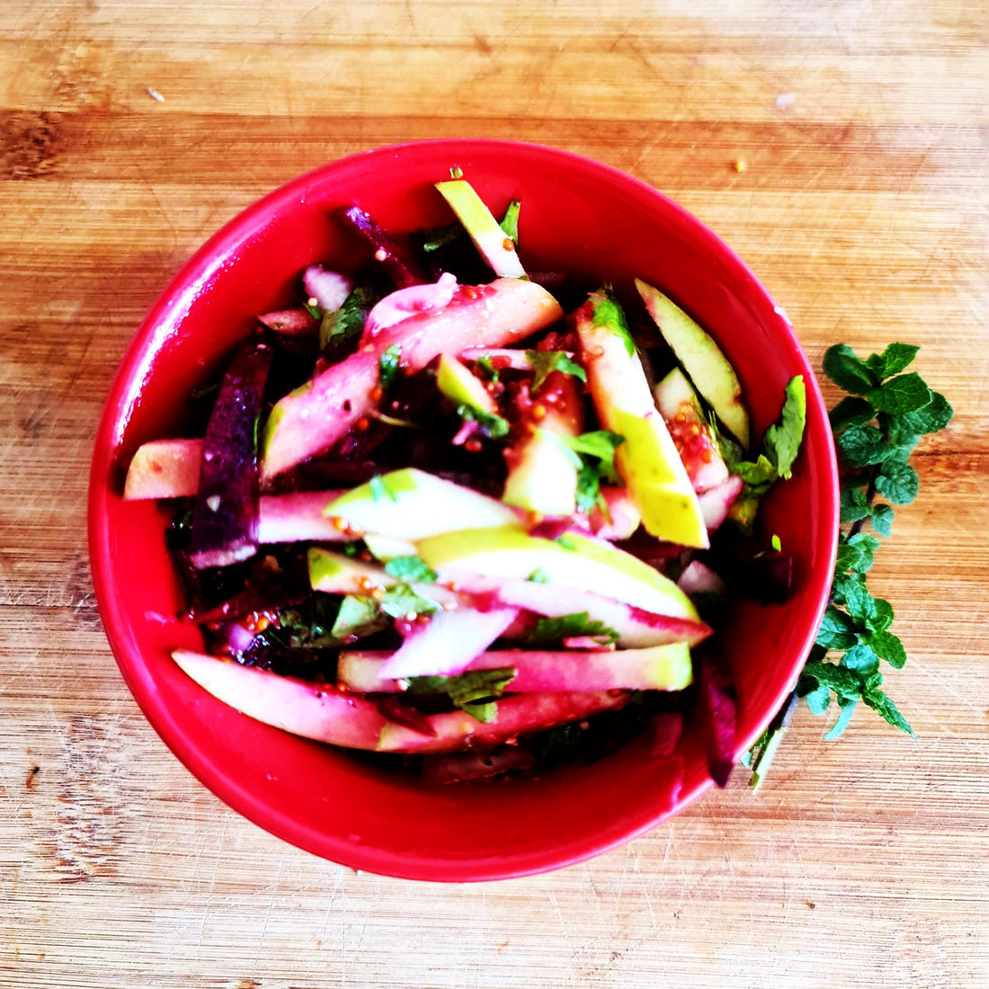 Organic apple and beet salad with special mustard dressing and mint from the home garden. In the photo, it is served in a red Chinese bowl.