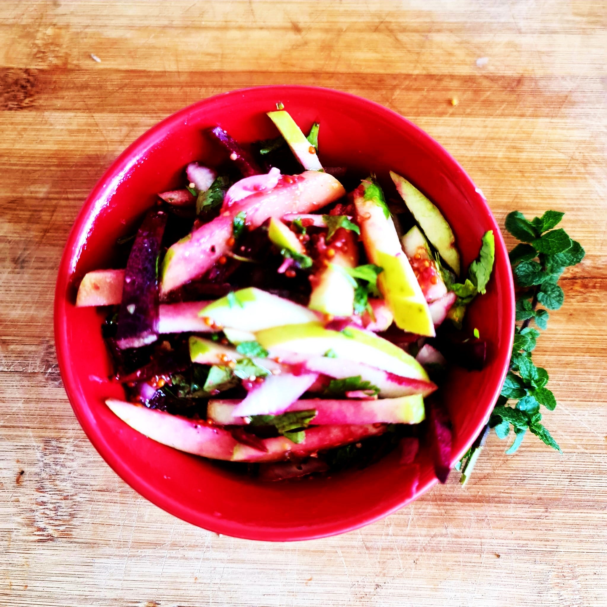 Organic apple and beet salad with special mustard dressing and mint from the home garden. In the photo, it is served in a red Chinese bowl.