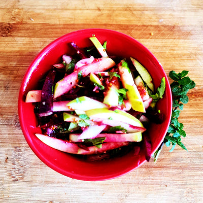 Organic apple and beet salad with special mustard dressing and mint from the home garden. In the photo, it is served in a red Chinese bowl.